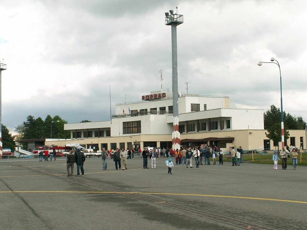 Budova terminálu letiska v Poprade s nápisom POPRAD, pred ňou skupina ľudí na letiskovej ploche