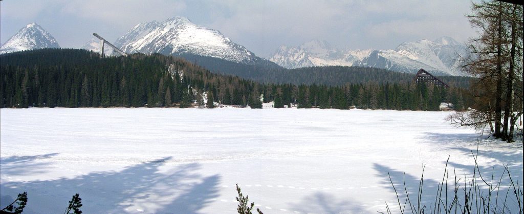 Zamrznuté a zasnežené Štrbské Pleso, v pozadí zasnežené štíty Vysokých Tatier a skokanské mostíky